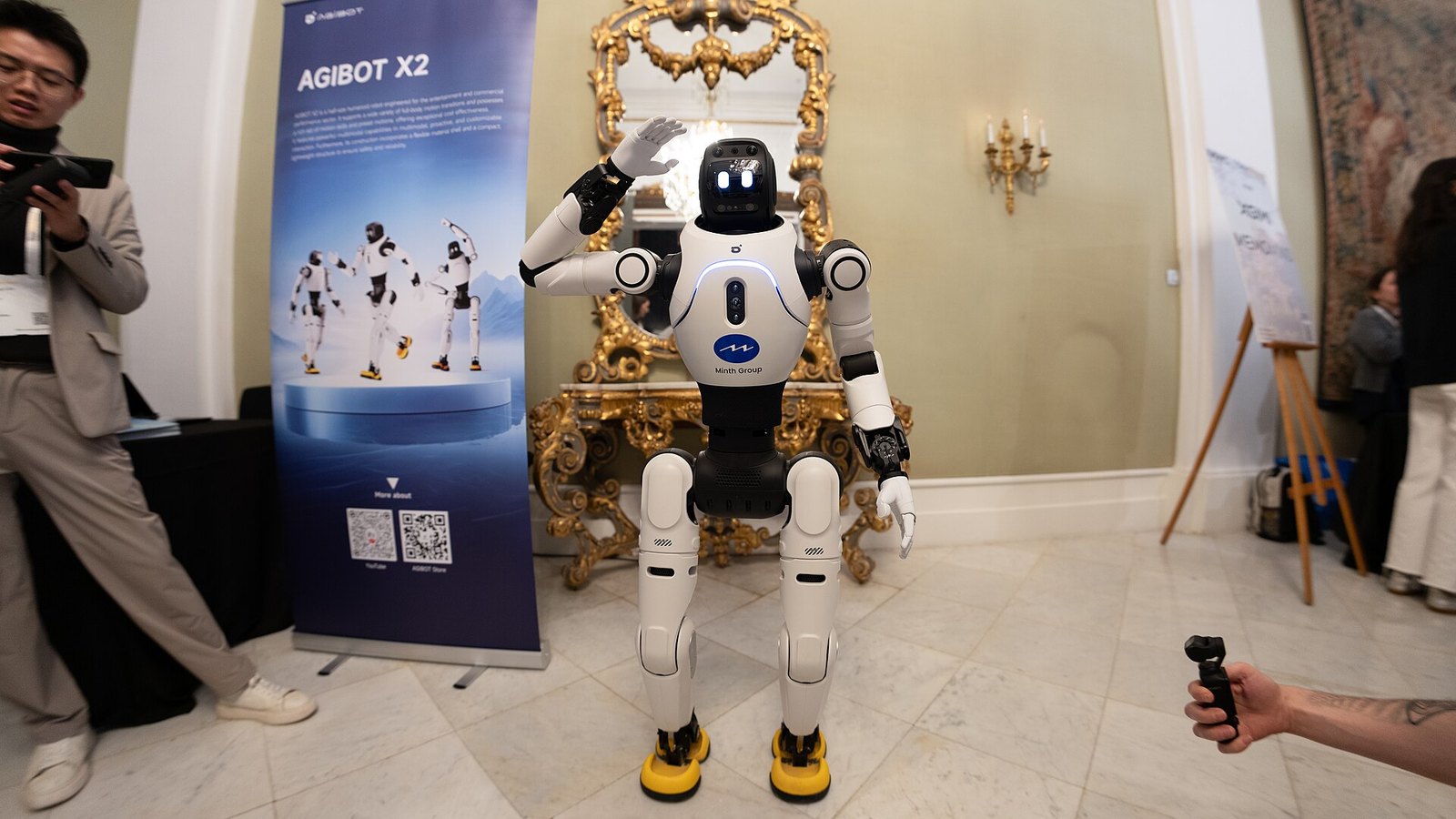 Humanoider Roboter AgiBot X2 steht winkend zwischen Besuchern in einem Ausstellungsraum